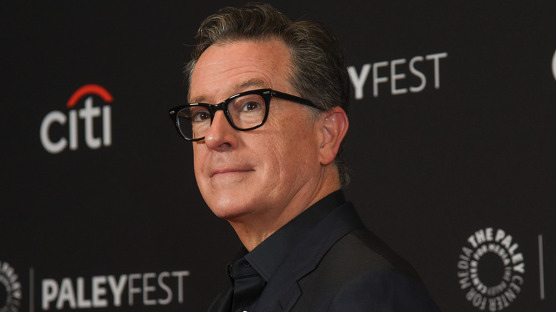 Stephen Colbert posing in black frame glasses at PaleyFest 2024