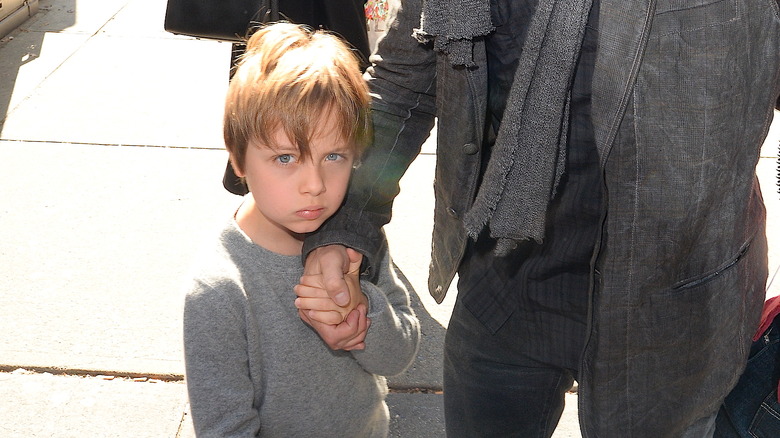 Close-up of young Knox Jolie-Pitt looking into camera on street holding Brad Pitt's hand