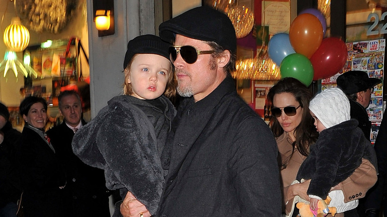 Brad Pitt holding baby Knox and Angelina Jolie holding baby Vivienne walking on street surrounded by onlookers