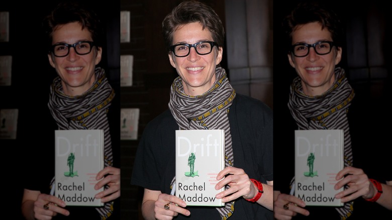 Rachel Maddow holding a copy of her book Drift