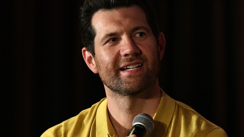 Billy Eichner holds a microphone in a yellow shirt