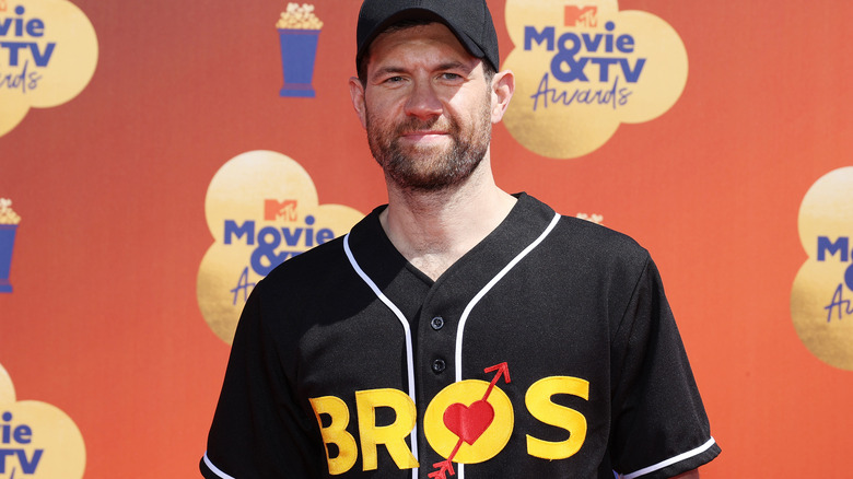 Billy Eichner holds a microphone in a yellow shirt