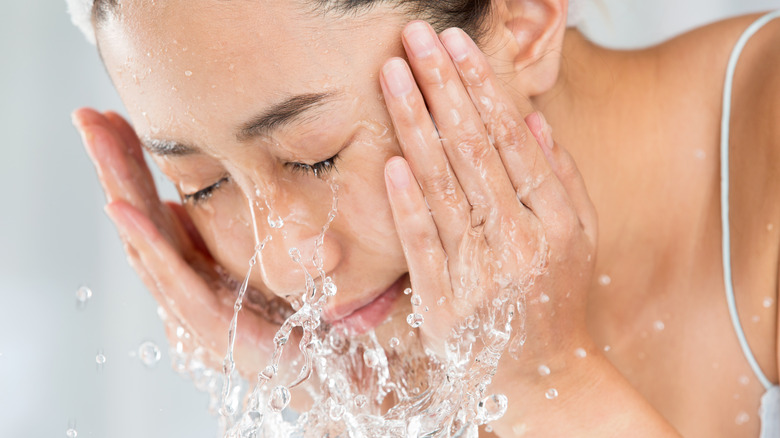 Woman with eyes closed splashing cold water on her face