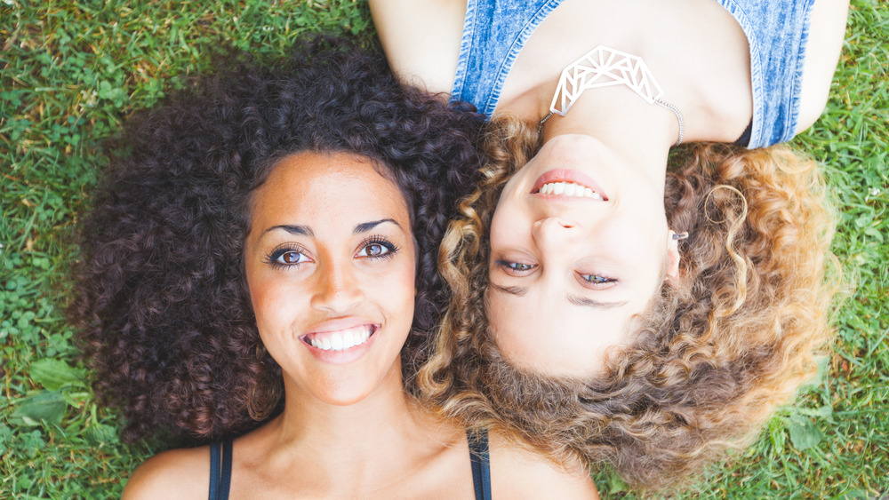 Two women with curly hair, laying on grass