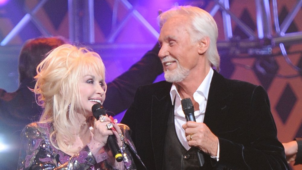 Dolly Parton and Kenny Rogers smiling at one another on stage