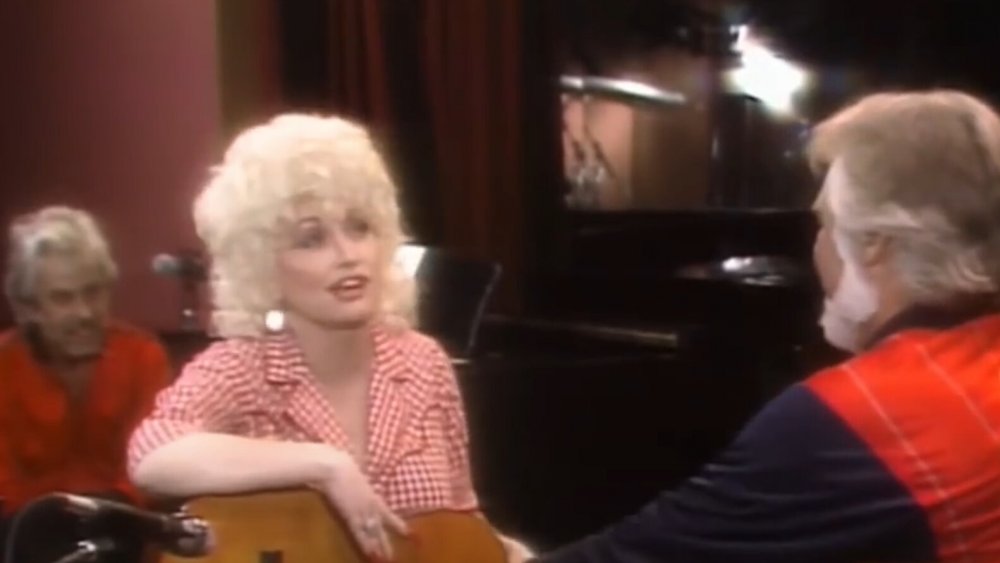 Dolly Parton holding a guitar, talking to Kenny Rogers