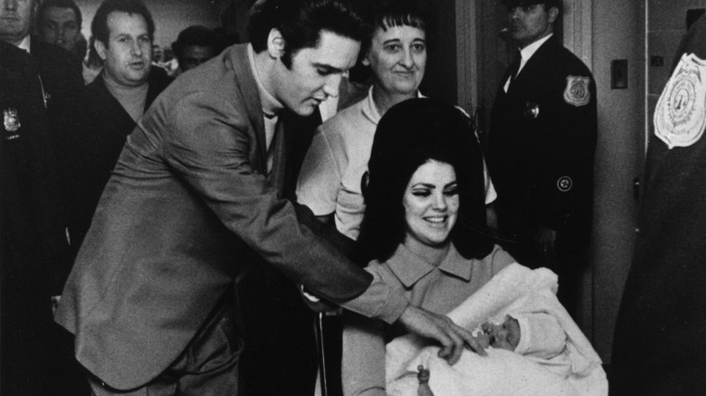 Elvis Presley touching baby in Priscilla's arms 