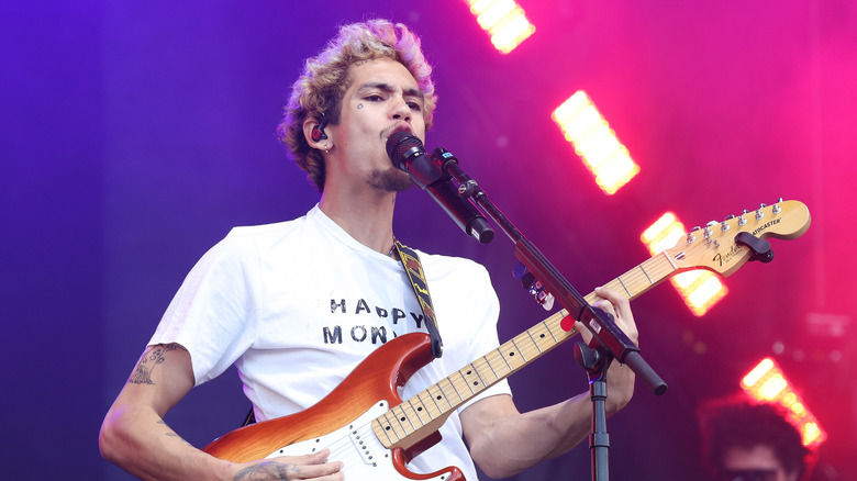 Dominic Fike playing guitar and singing into a microphone