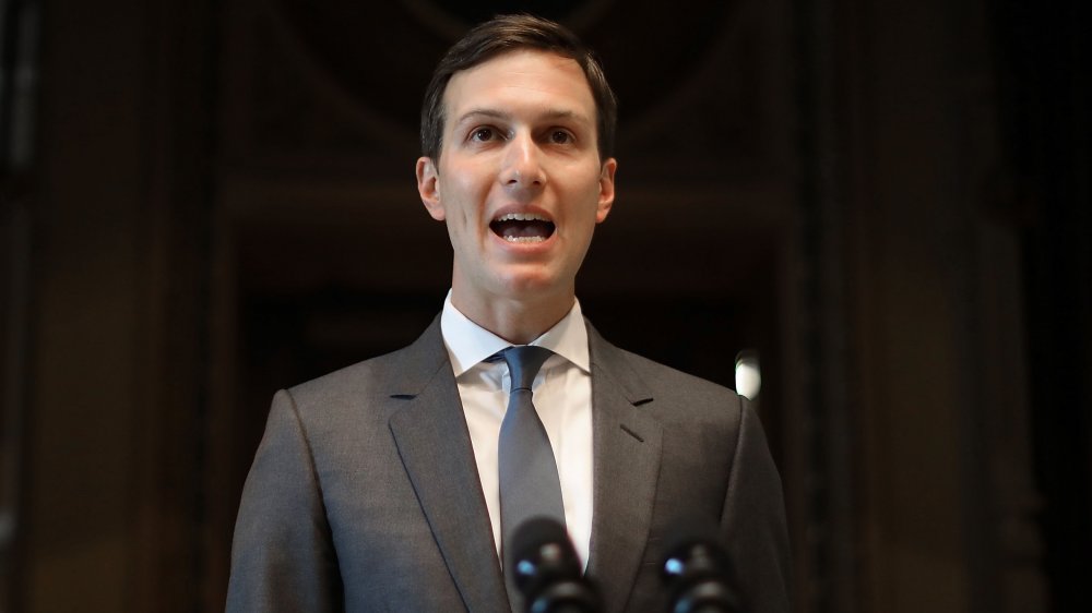 Jared Kushner in a gray suit, speaking at a podium