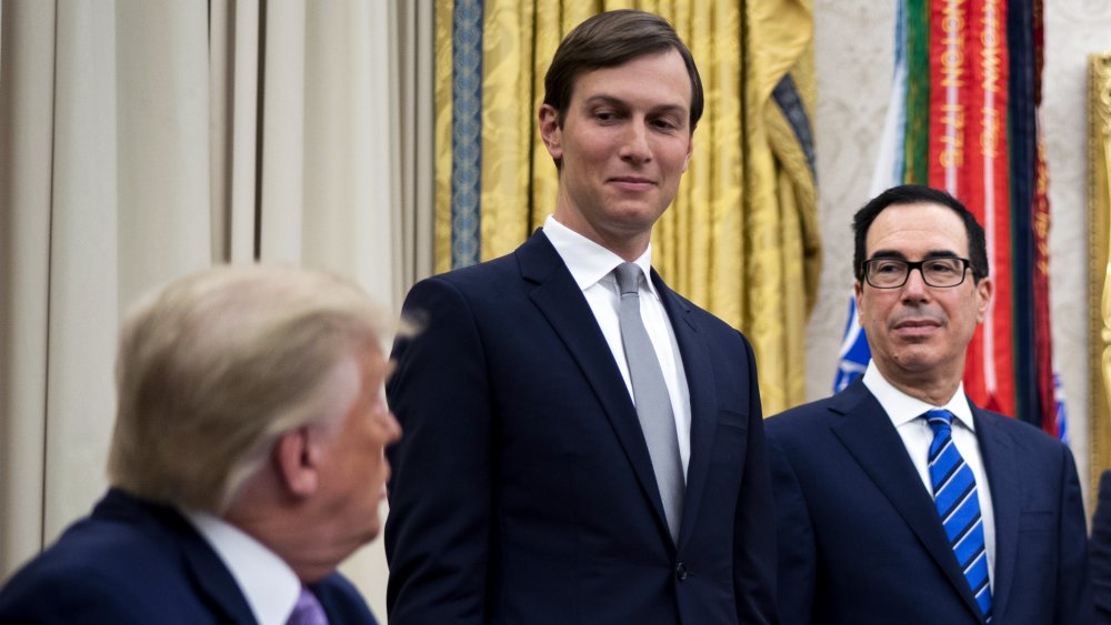 Jared Kushner smirking while looking down at Donald Trump