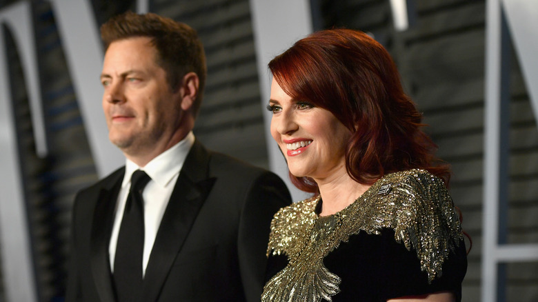 Mullally, in focus, smiles on red carpet while Offerman poses behind her