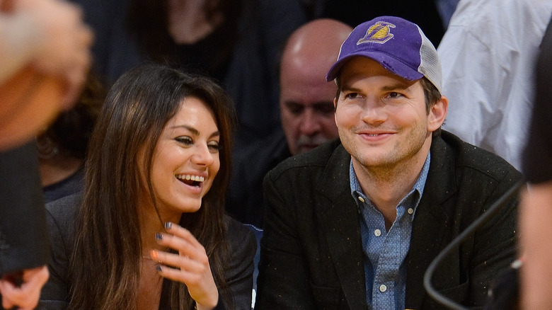 Ashton Kutcher and Mila Kunis smiling courtside