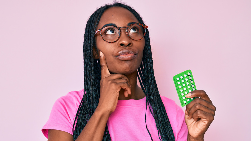 Thinking woman holding birth control