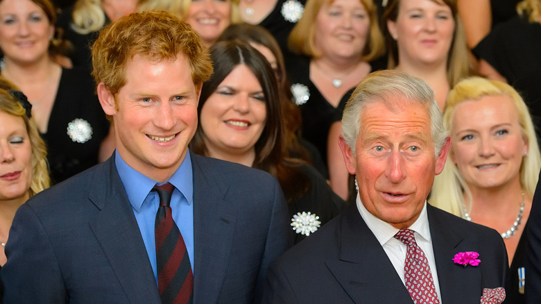 Prince Harry smiling with King Charles in a crowd