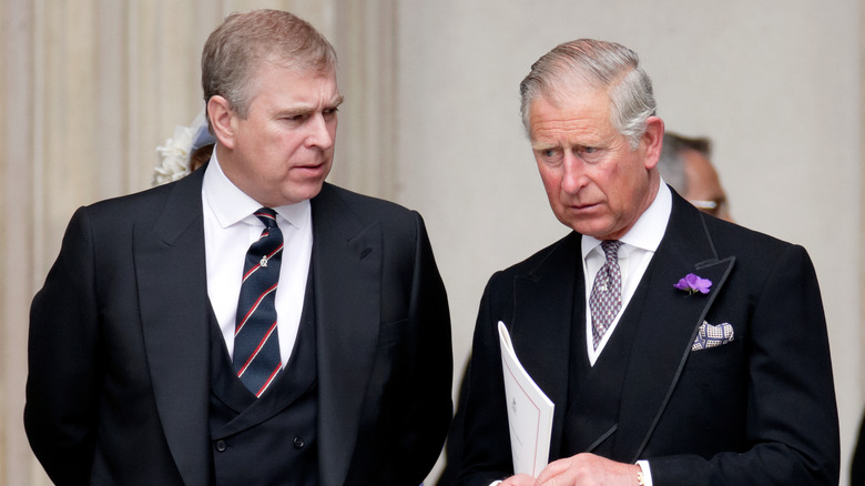 Prince Andrew looking concerned while speaking with Prince Charles