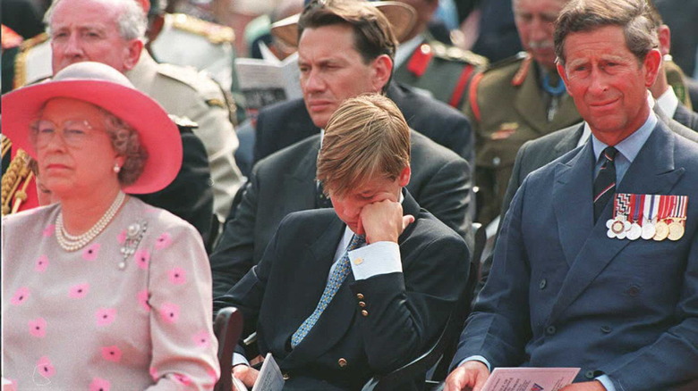 Prince William with his head in his hand beside Prince Charles