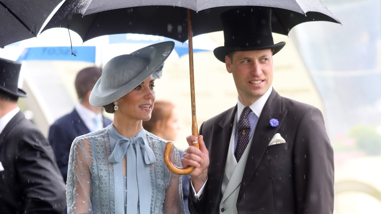 Princess Catherine & Prince William standing under umbrella in rain