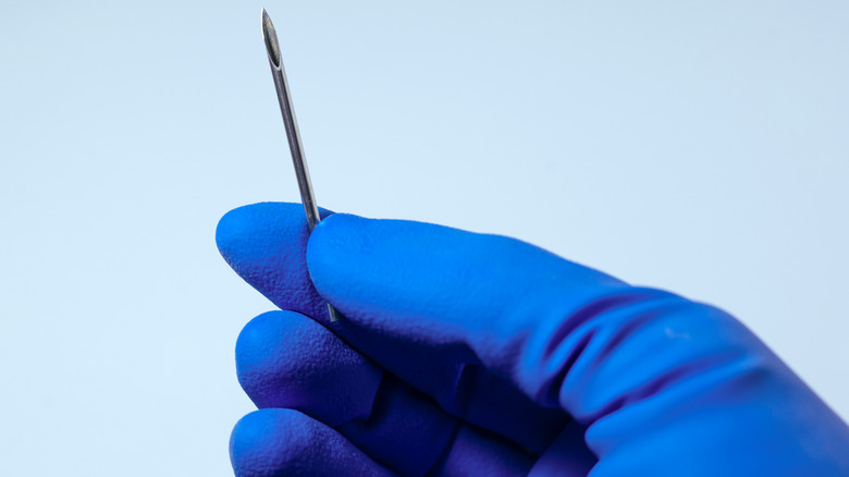 A gloved hand holding a piercing needle