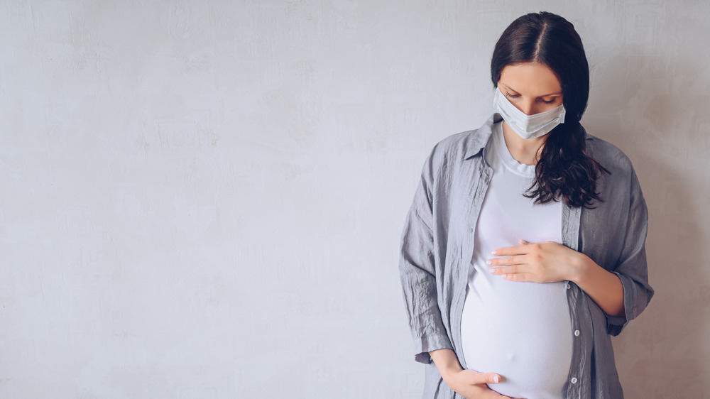 masked woman who is pregnant holding belly