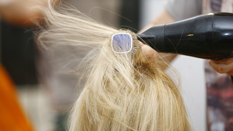 hairstylist drying short blond hair with blowdryer and comb