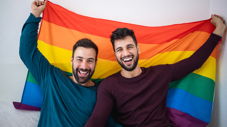 Two men hold the rainbow flag above them