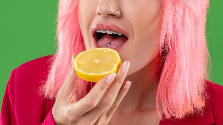 Woman with pink hair and tongue piercing eating lemon