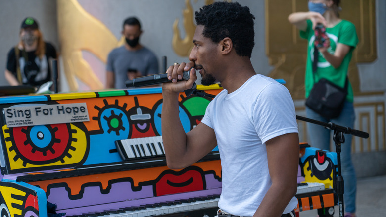 Musician Jon Batiste singing and sitting in front of a piano