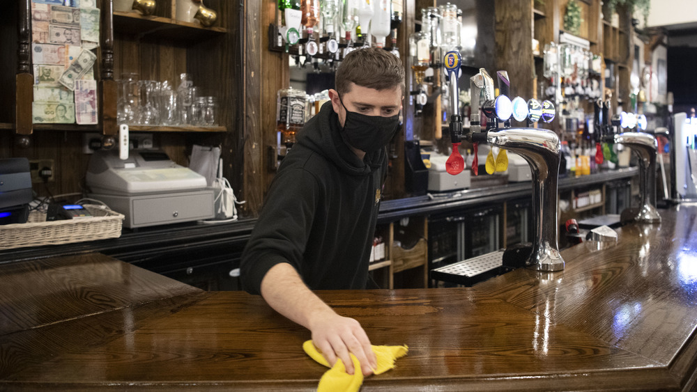 Masked bartender cleans a bartop 