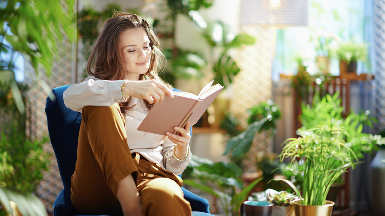A woman reading a book surrounded by plants 