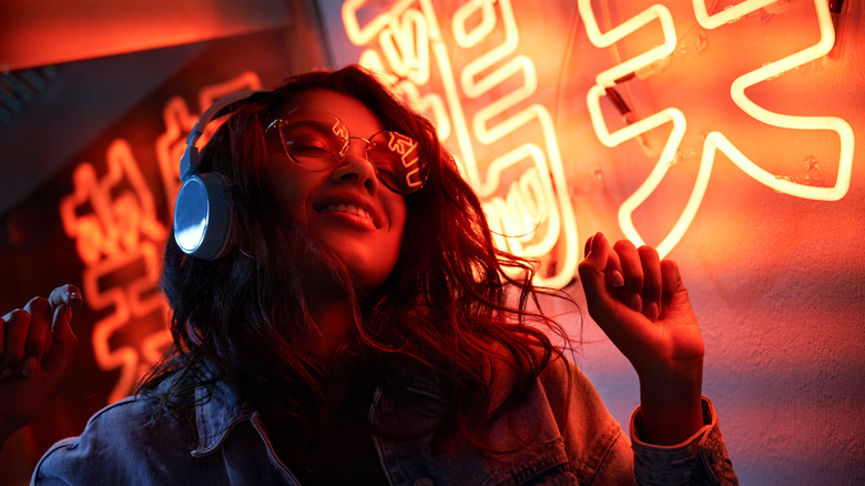 A woman wearing headphones by a neon sign 