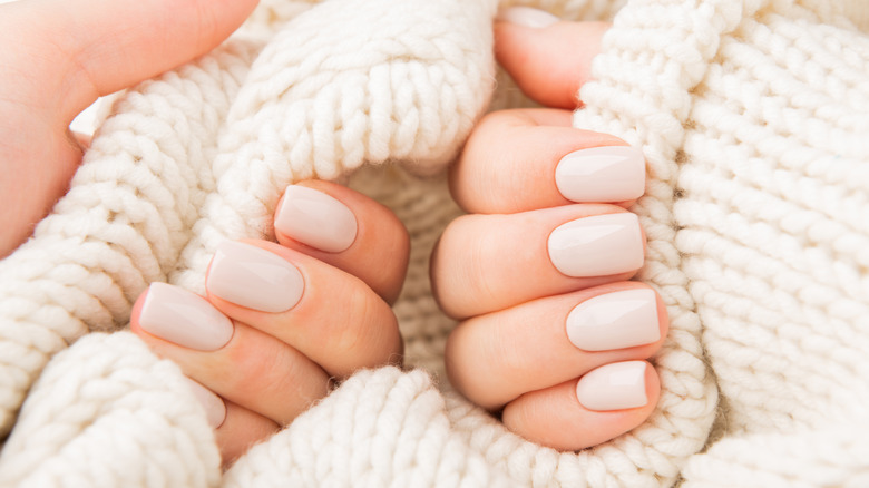 Hands against a woven, white background, featuring light beige gel nails