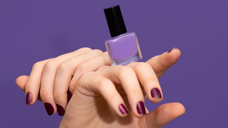 Hands with nails painted purple, holding purple nail polish