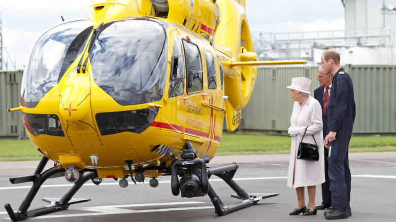 Pilot Prince William and Queen Elizabeth standing by a helicopter
