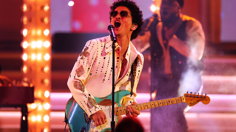 Bruno Mars in white jumpsuit playing guitar