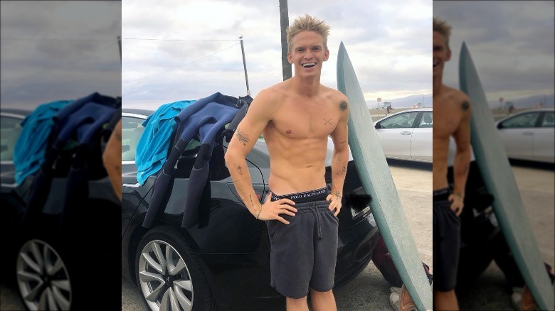 Cody Simpson leaning on his car with a surf board