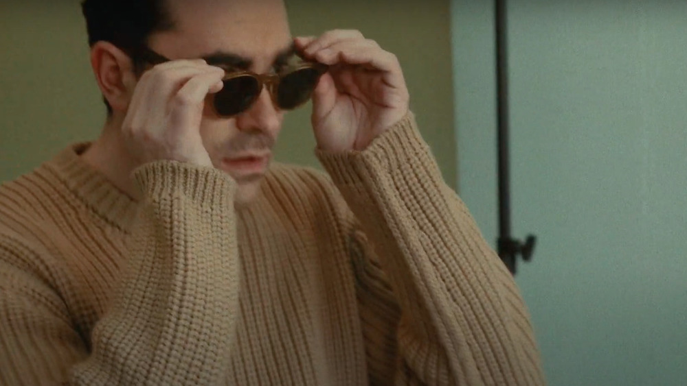 Dan Levy putting on a pair of sunglasses