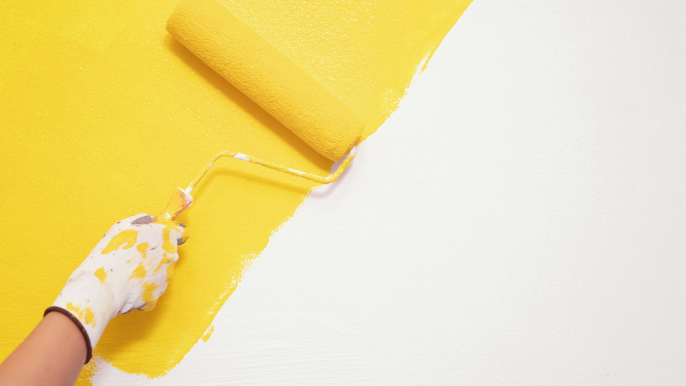 Person painting a wall yellow with a roller