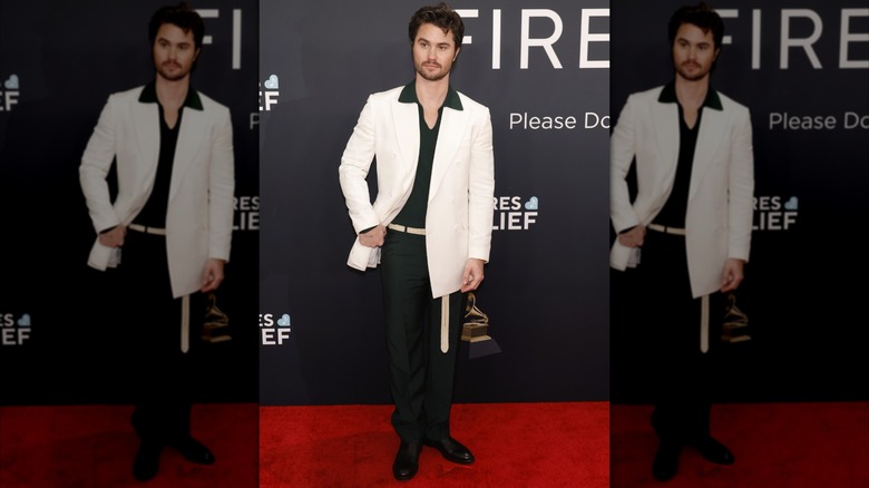 Chase Stokes posing on the red carpet in green outfit and white jacket