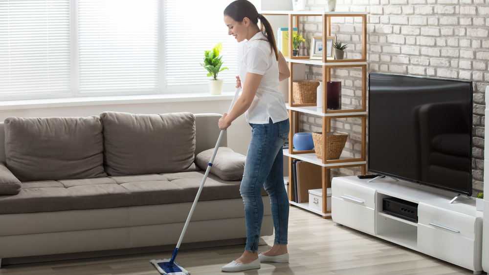 Woman dry mopping a hardwood floor while smiling.