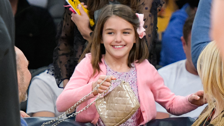 Child Suri Cruise smiling while carrying a gold purse