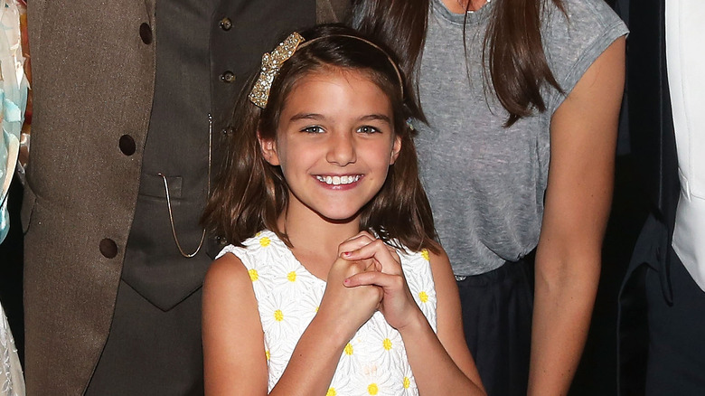 Child Suri Cruise smiling in a white dress 