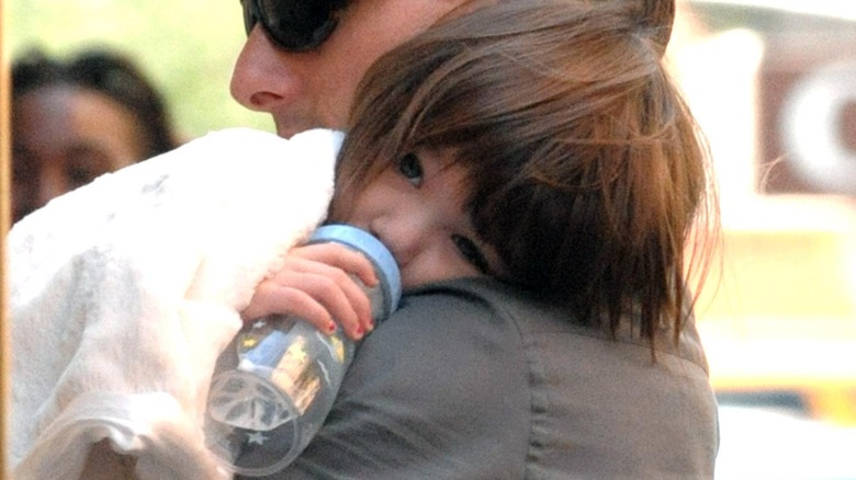 Baby Suri Cruise drinking from a bottle while carried by Tom Cruise 