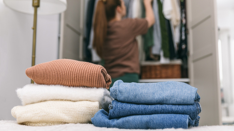 Woman looks through her closet, sweaters and jeans sit on her bed