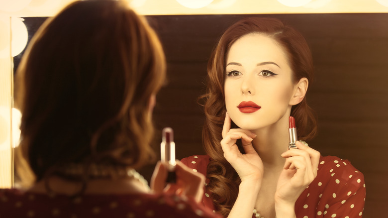 woman applying red lipstick in a mirror