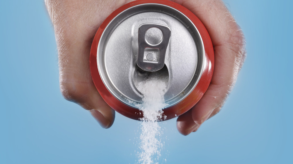 Hand pouring sugar from a soda can