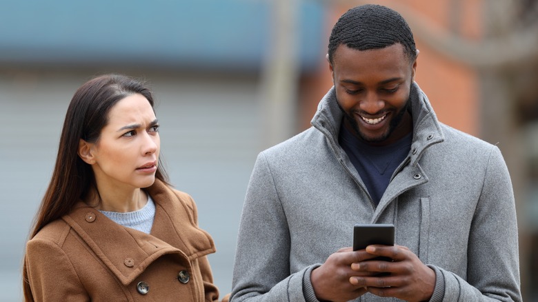 woman upset, man smiles at phone 