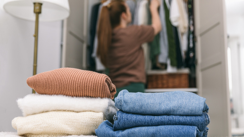 Person standing at closet, with sweaters and jeans on bed