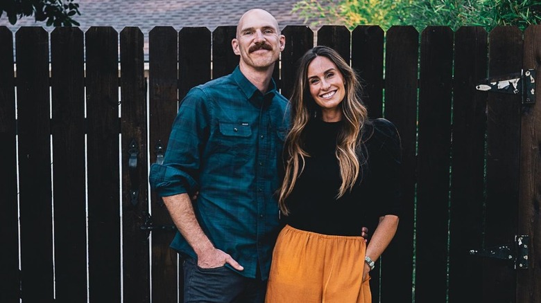 Bryan and Kim Wolfe posing together in front of a fence