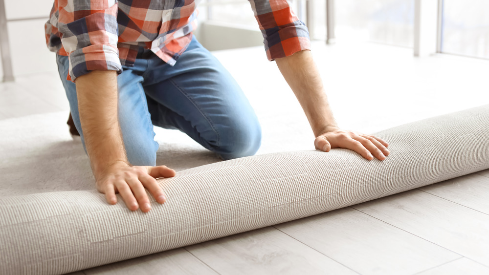 Man rolling out carpet on floor