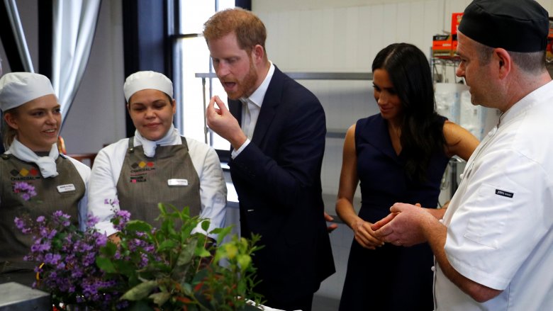 Meghan Markle standing beside Prince Harry as he eats